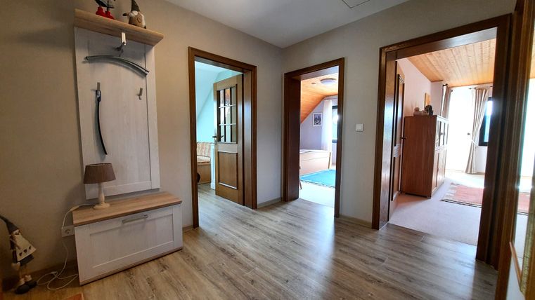 A bright hallway with wooden flooring and several doors leading to other rooms. The walls are in neutral colors and there is a small wooden cupboard.