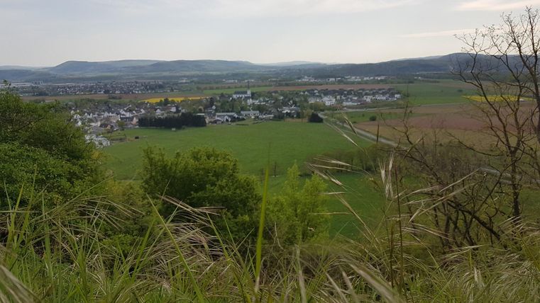 Eine malerische Landschaft mit sanften Hügeln und einem kleinen Dorf im Tal. Das Bild zeigt weite Felder und eine ruhige, natürliche Umgebung.