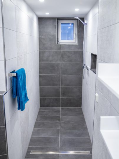 A modern shower with gray tiles and bright light. A blue towel hangs on the wall.