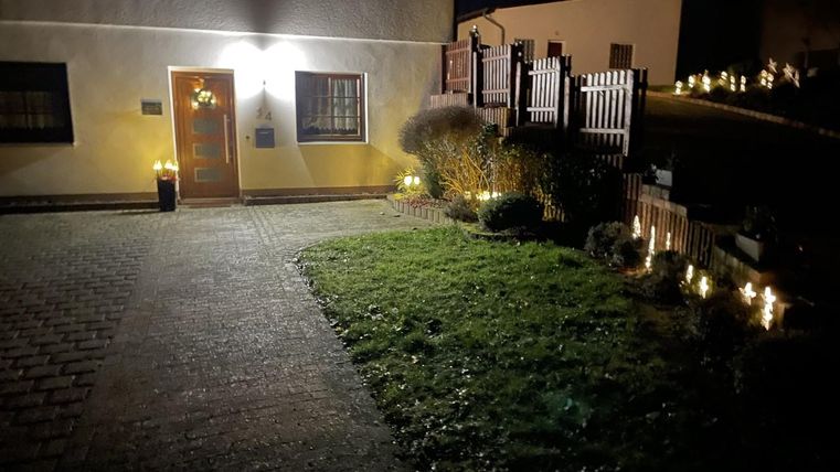 Een gezellige oprit naar een huis bij nacht, verlicht door warme lichten. Het gras is goed onderhouden en er is een decoratieve hek.