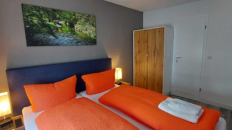Ein modernes Schlafzimmer mit orangefarbenen Kissen und Decken. An der Wand hängt ein Bild eines grünen Flusses in der Natur.