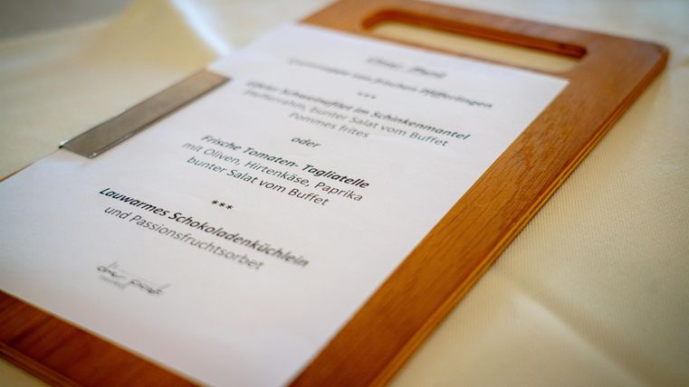 Ein Flyer auf einem Holztablett mit Informationen über ein Buffet. Die Speisen sind auf der Karte aufgelistet.