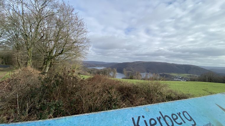 Een uitzicht op de heuvels en de vallei van Kierberg. Op de voorgrond is een informatiebord zichtbaar dat de verhoging aangeeft.