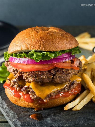 Ein saftiger Burger mit zwei Rindfleischpattys, Cheddar-Käse, frischem Salat, Tomaten und Zwiebeln. Dazu gibt es knusprige Pommes frites auf einem schwarzen Stein.