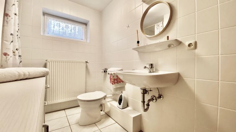 Ein kleines Badezimmer mit weißen Fliesen. Es verfügt über eine Toilette, ein Waschbecken und einen Spiegel.