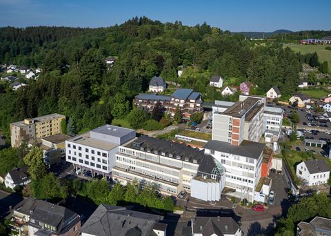 Eine Luftaufnahme eines modernen Gebäudekomplexes in einer ländlichen Umgebung. Im Hintergrund sind Hügel und grüne Bäume zu sehen.