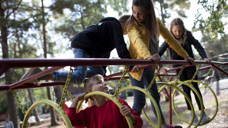 Eine Gruppe von Kindern spielt auf einem Spielplatz. Sie klettern an einem Spielgerät mit Ringen und haben Spaß zusammen.