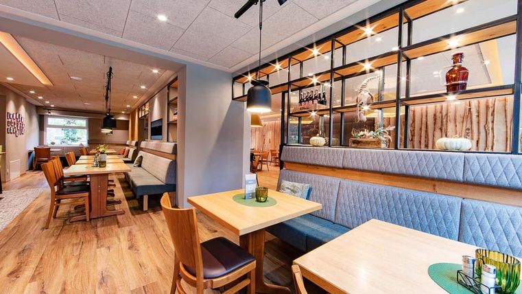 Ein modernes Restaurant mit warmem Holzboden und gemütlichen Tischen. Die Wände sind dekoriert mit eleganten Regalen und sanftem Licht.