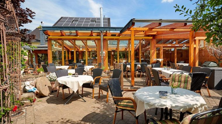 Ein einladendes Restaurant mit Außenbereich und Holzkonstruktion. Die Tische sind für Gäste vorbereitet, umgeben von einer angenehmen Atmosphäre.