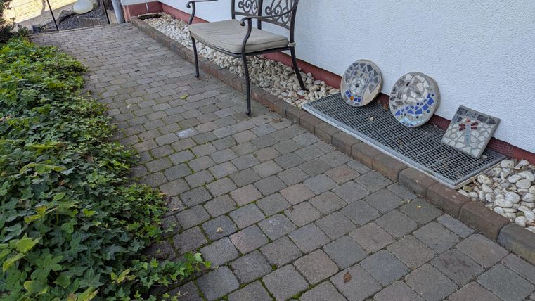 Een geplaveide terras met een decoratieve bank en kleurrijke borden. Aan de linkerkant groeit een groene plant.