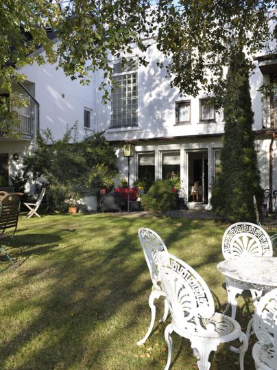 Ein schöner Garten mit einem gepflegten Rasen und weißen Gartenmöbeln. Im Hintergrund ist ein helles Haus mit großen Fenstern zu sehen.