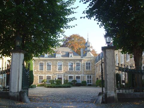 Een elegant gebouw met grote ramen en een mooie tuin. De ingang wordt geflankeerd door hoge bomen.