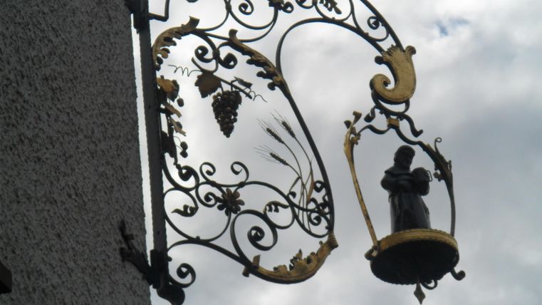 An artistic iron swing with golden embellishments and a statue. Clouds can be seen in the background.