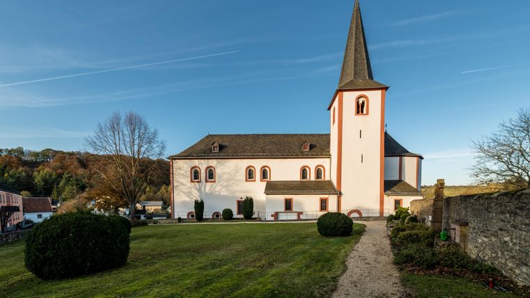 Das Kloster Niederehe mit seinem markanten Kirchturm und gepflegtem Rasen im Vordergrund, umgeben von herbstlicher Landschaft.