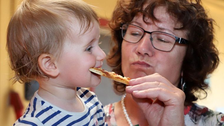 A small child is being fed by an adult. Both have friendly facial expressions and are enjoying the moment together.