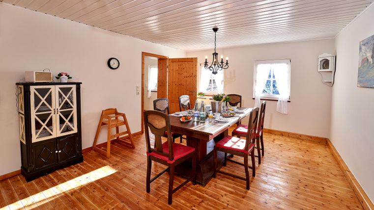 An inviting dining area with a large table and chairs. The room has a warm wooden floor and a bright, friendly atmosphere.