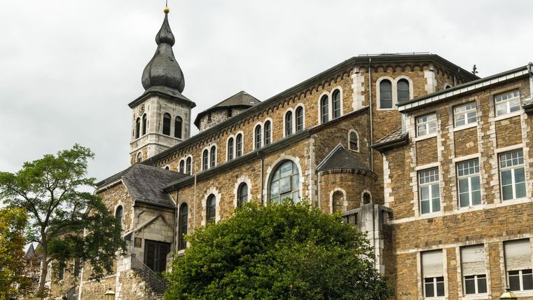 Eine beeindruckende Kirche mit einem hohen Turm und einer interessanten Architektur. Umgeben von Bäumen und historischen Gebäuden.