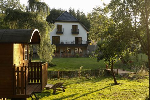 An idyllic house with a balcony, surrounded by a well-maintained garden. In the foreground stands a small wooden structure that invites relaxation.