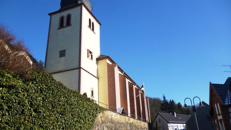 Ein historisches Gebäude mit einem hohen Turm und einer klaren blauen Himmel im Hintergrund. Die Fassade des Hauses ist teilweise mit grünen Pflanzen bedeckt.