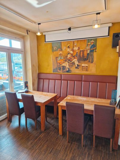 A cozy restaurant with wooden tables and leather benches. A colorful mural of musicians hangs on the wall.