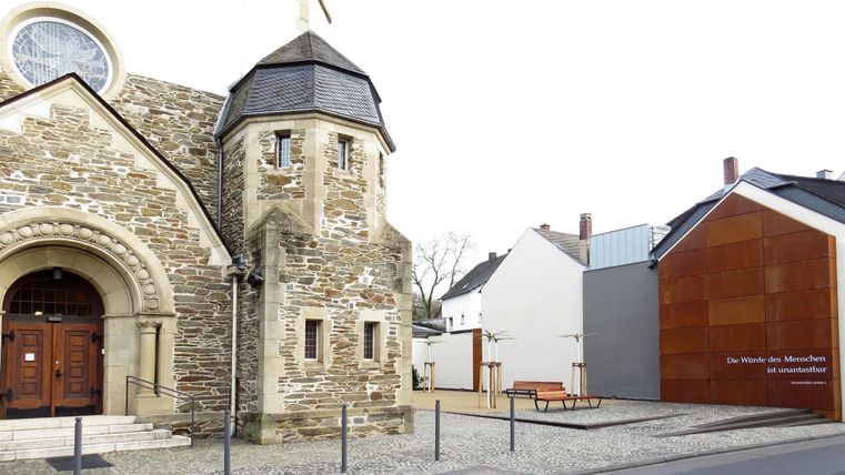 Ein historisches Gebäude mit einer markanten Rundkirche und einem modernen Bau daneben. Die Fassade ist aus Stein und Holz, die Straße ist ruhig und gut gestaltet.