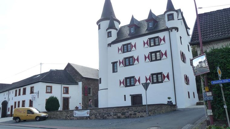 Een charmant, historisch gebouw met torens en kleurrijke vensters. Het staat op een straatzijde hoek in een klein stadje.