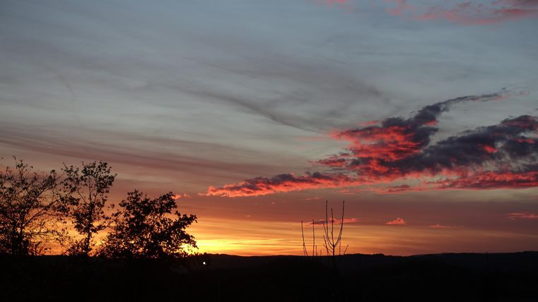 A beautiful sunset with colorful clouds in the sky. Silhouettes of trees frame the landscape.