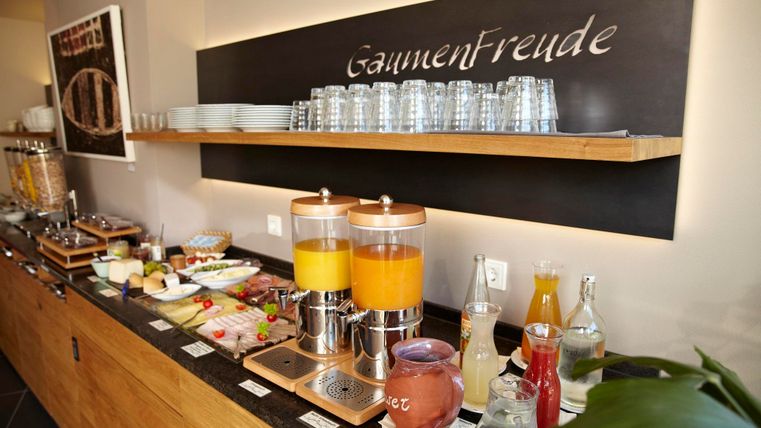 A breakfast buffet with fresh juices, various dishes, and glasses. The table is neatly and invitingly decorated.