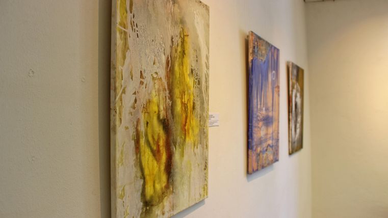 Eine Galerie mit verschiedenen modernen Kunstwerken an der Wand. Die Bilder zeigen abstrakte Muster in verschiedenen Farben.