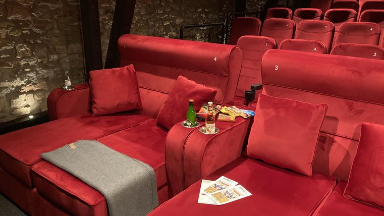 A cozy cinema with red seats and stylish couch elements. Snacks and drinks are ready on the table.