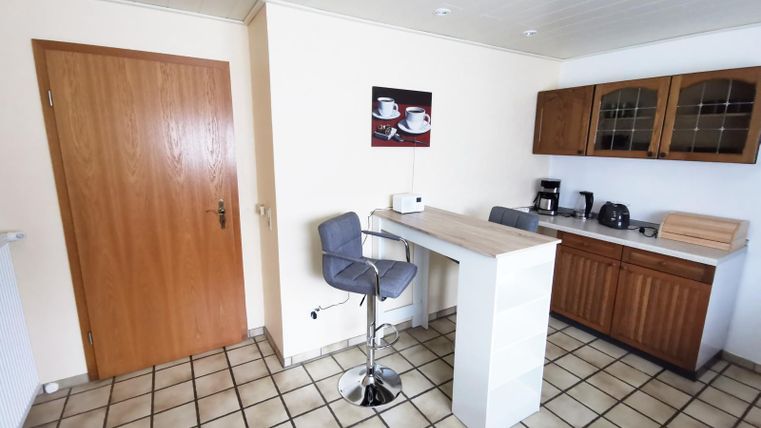 A modern kitchen with bright wooden furniture and a small bar counter. On the wall hangs a picture of coffee cups.