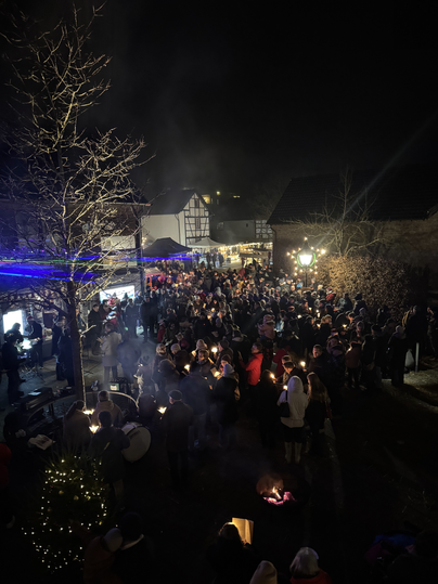 A large crowd gathers at an event in the evening. Lights and smoke create a festive atmosphere.