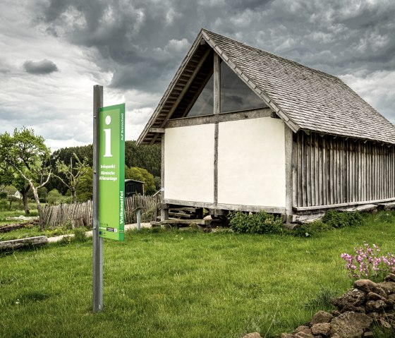 Ein Holzgeb&auml;ude mit Schindeldach neben einem gr&uuml;nen Infoschild in l&auml;ndlicher Umgebung. Der Himmel ist bew&ouml;lkt., &copy; Eifel Tourismus GmbH, Dominik Ketz