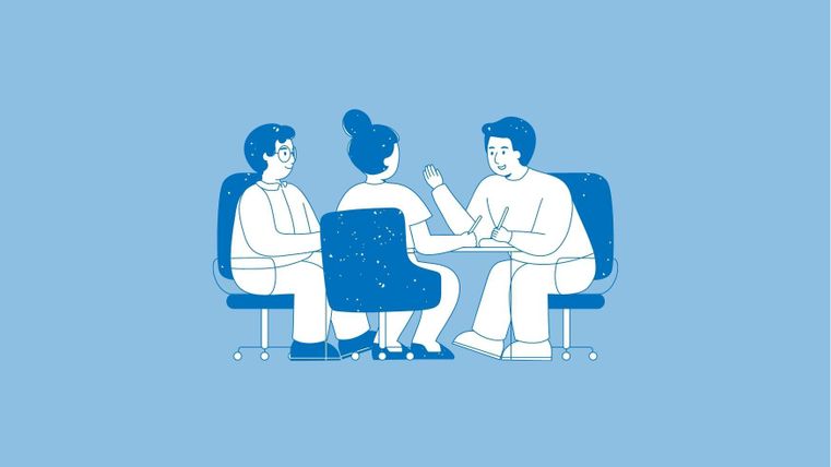 Drei Personen sitzen an einem Tisch und sprechen miteinander. Sie scheinen eine Diskussion oder ein Beratungsgespräch zu führen.