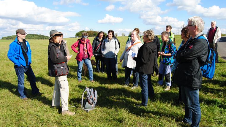 Gruppe von Menschen auf einer Wiese bei einer Wanderung unter blauem Himmel.