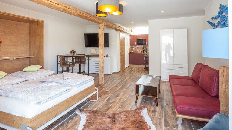 Ein modernes Zimmer mit einem Doppelbett, einer roten Couch und einem Fernseher an der Wand. Die helle Einrichtung schafft eine einladende Atmosphäre.