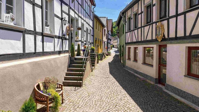 Eine malerische Straße mit Fachwerkhäusern und gepflastertem Boden. Die Umgebung ist hell und einladend, mit klarer Blauer Himmel.