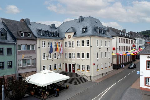 A historical building with traditional architecture is located on a quiet street. Several flags are visible, and a sun umbrella stands in front of the building.