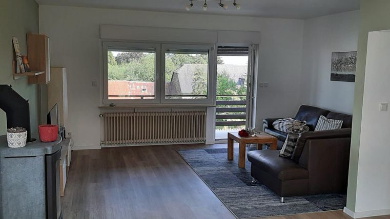 Ein helles Wohnzimmer mit einem gemütlichen Sofa und großen Fenstern. Der Raum hat einen modernen Touch und ist gut möbliert.