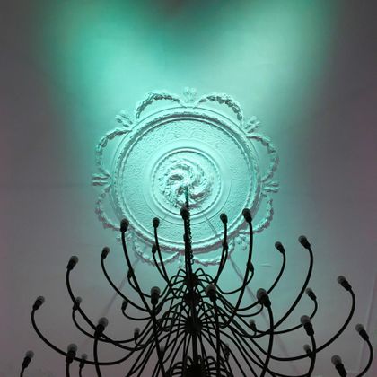 Eine elegante Deckenleuchte mit geschwungenem Design und einem sanften, grünen Licht. Der Lichteffekt hebt die aufwendige Stuckleiste hervor.