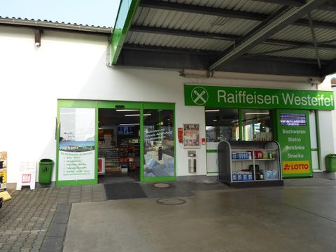 A market with an entrance area in green colors. Billboards and shelves are visible, displaying various products.