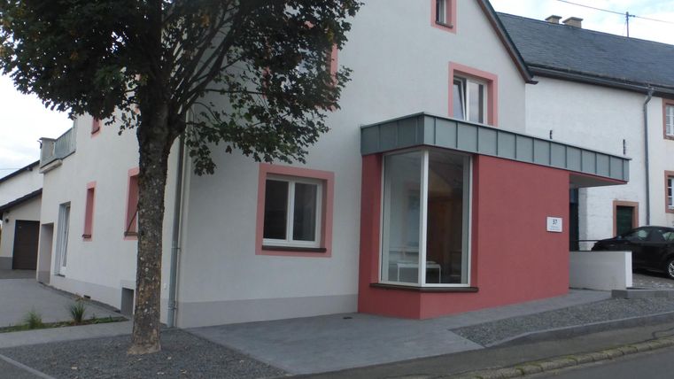 Ein modernes Haus mit roten Akzenten und großen Fenstern. Es steht an einer ruhigen Straße und hat einen schlichten, einladenden Eingangsbereich.