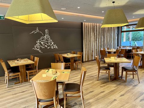 Ein modernes Restaurant mit Holztischen und Stühlen. Die Wand zeigt eine stilisierte Zeichnung einer Burg und die Beleuchtung ist angenehm.