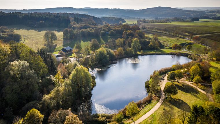 Aerial view: view of the lake with hiking/cycling path along the lake. Trees surround the lake.