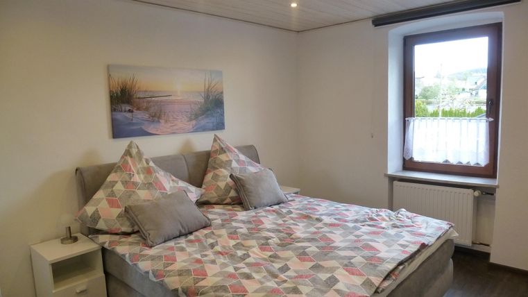 Ein gemütliches Schlafzimmer mit einem großen Bett und dekorativen Kissen. Ein Fenster mit Ausblick und ein Landschaftsbild an der Wand ergänzen den Raum.