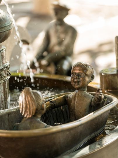 Eine schöne Bronzestatue von zwei Kindern in einer Badewanne. Wasser sprudelt aus der Umgebung und schafft eine lebendige Atmosphäre.