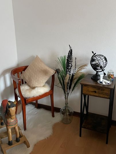 Een gezellige woonkamer met een houten stoel, een kussen en een kleine globe-decoratie. Naast de stoel staat een vaas met planten en een kleine tafel.