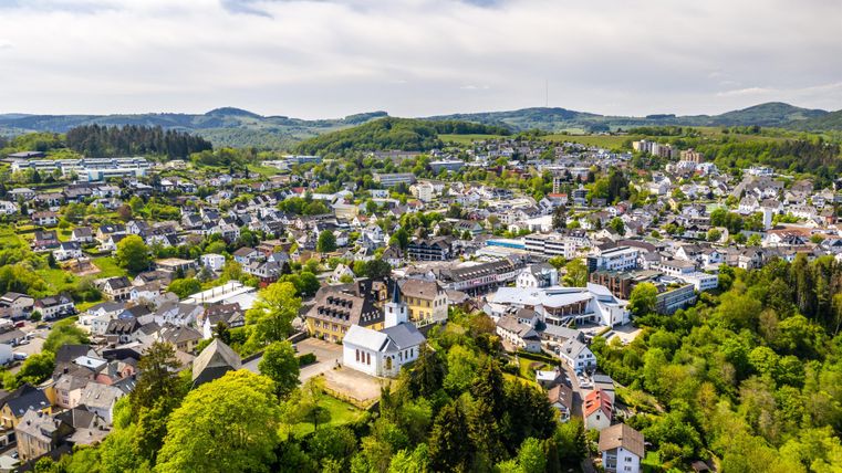 Een schilderachtig uitzicht op een stad omringd door groene heuvels en bomen. De gebouwen zijn goed verdeeld en het landschap is uitnodigend.