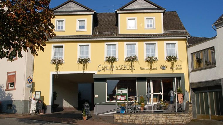 A yellow building with a café on the ground floor. Flower boxes hang in front of the windows, and the façade is friendly and inviting.