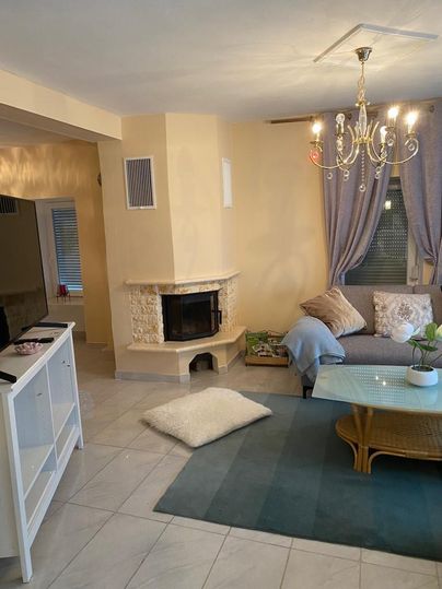 Ein gemütliches Wohnzimmer mit einem Kamin, einer Couch und einem Couchtisch. Der Raum hat helle Farben und eine elegante Deckenleuchte.